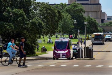 Students crossing street with smart shuttle in background.